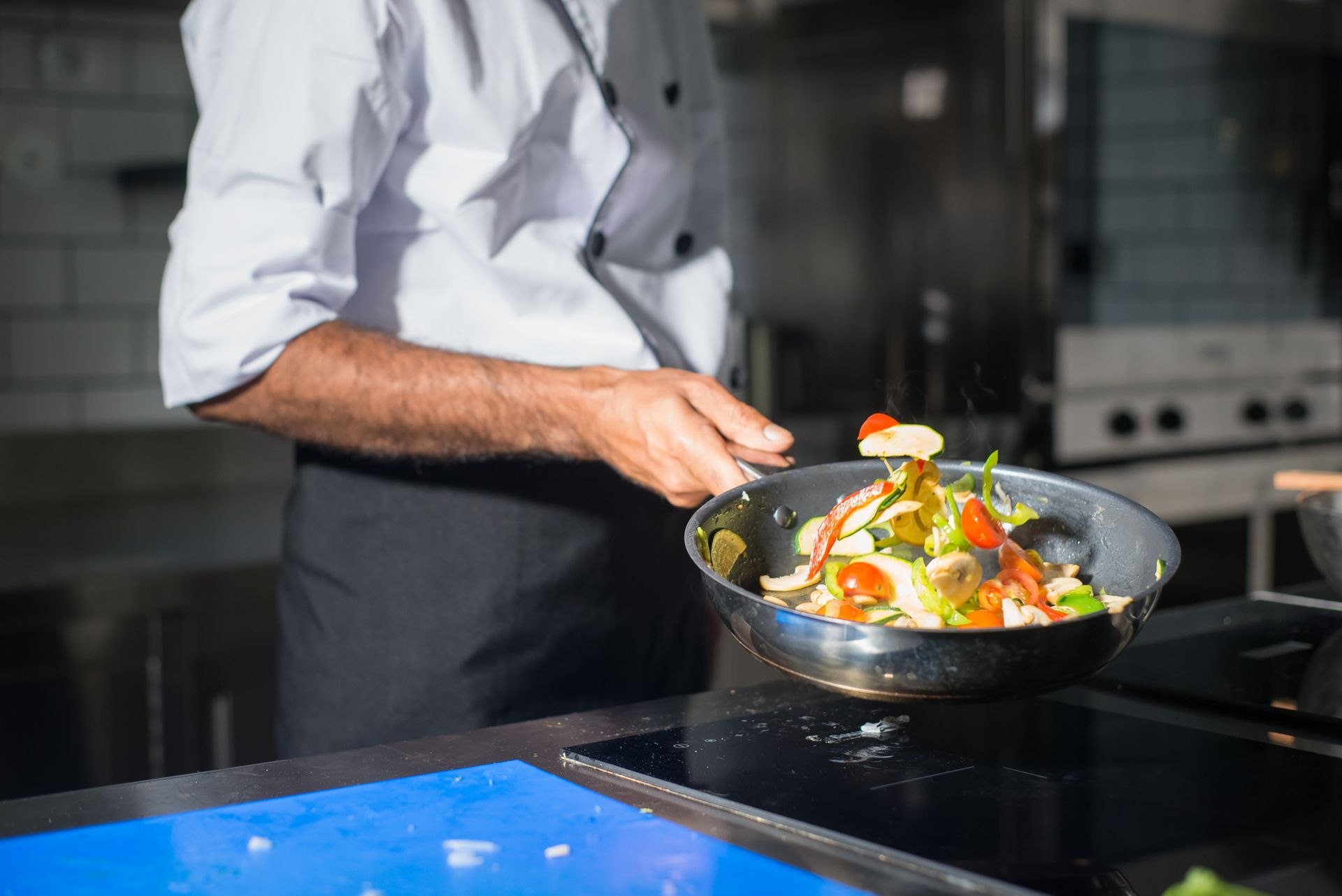 Profissional salteando vegetais em uma frigideira na cozinha de um restaurante