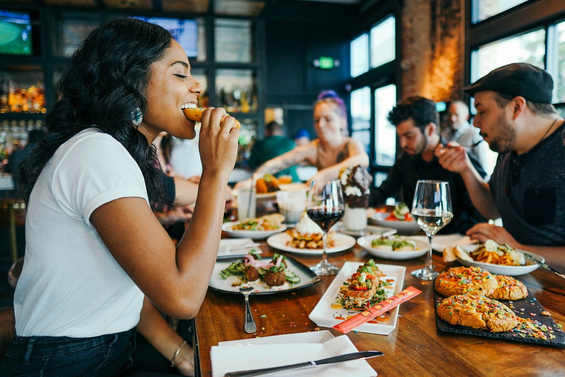 Quatro pessoas compartilham uma refeição à mesa de um restaurante, com vários pratos e copos de vinho
